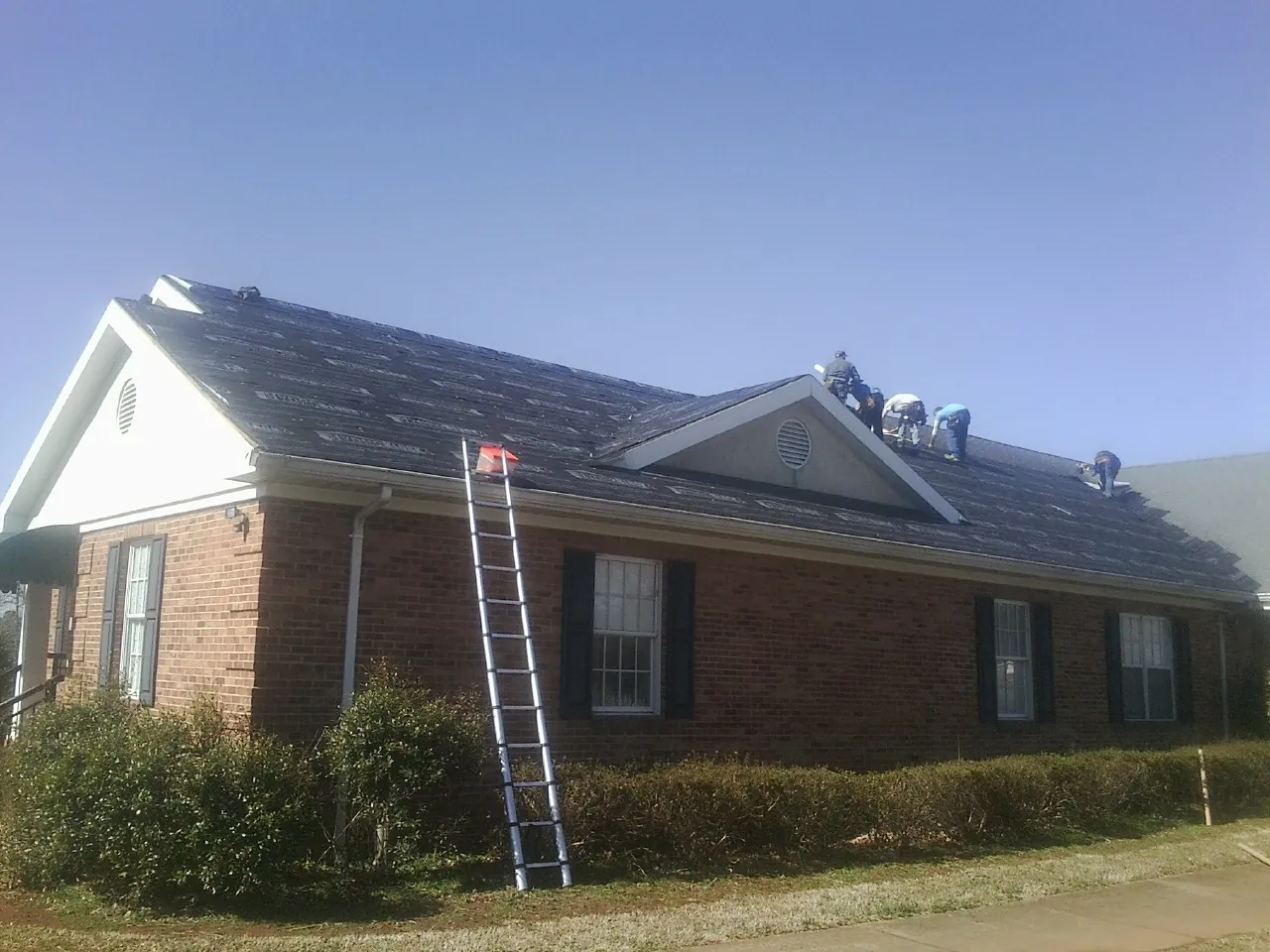 Crew tearing shingles off a brick ranch roof with a ladder set — Emergency Roof Repair work by our crew in Register
