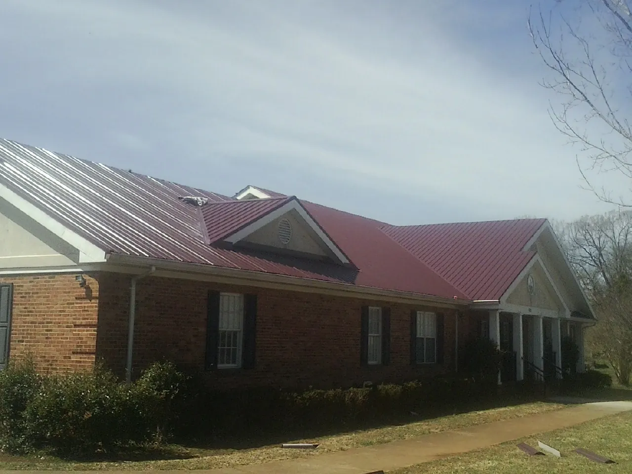 Red metal roof with gabled entries on a long brick building, from a Hail Damage Roof Repair job in Register