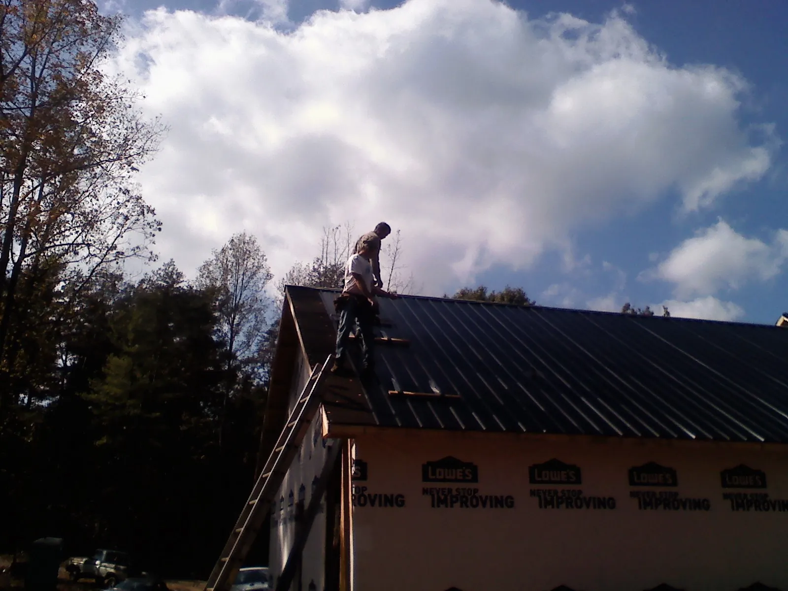 Roofer fastening dark metal panels high against a cloudy sky, from a Roof Inspection job in Register